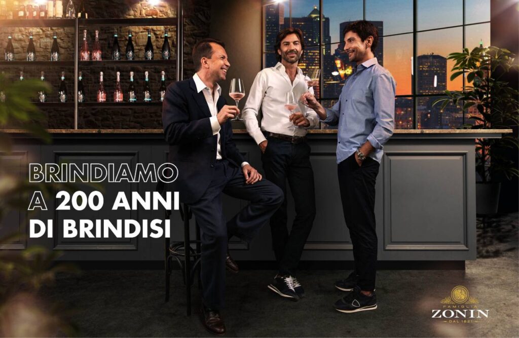 Tre uomini in abbigliamento business brindano con calici di vino rosato in una lounge con skyline cittadino sullo sfondo