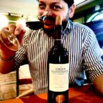 Uomo con camicia a righe assaggia vino rosso Groot Constantia davanti a un calice, espressione entusiasta