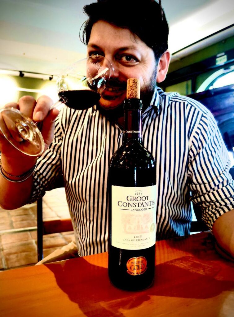 Uomo con camicia a righe assaggia vino rosso Groot Constantia davanti a un calice, espressione entusiasta