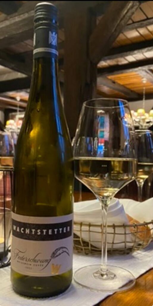 Bottiglia di vino bianco Wachtstetter con etichetta blu e bicchiere di vino servito a tavola