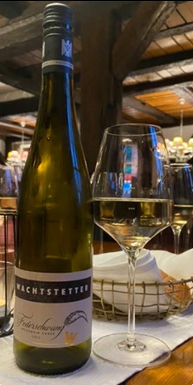 Bottiglia di vino bianco Wachtstetter con etichetta blu e bicchiere di vino servito a tavola